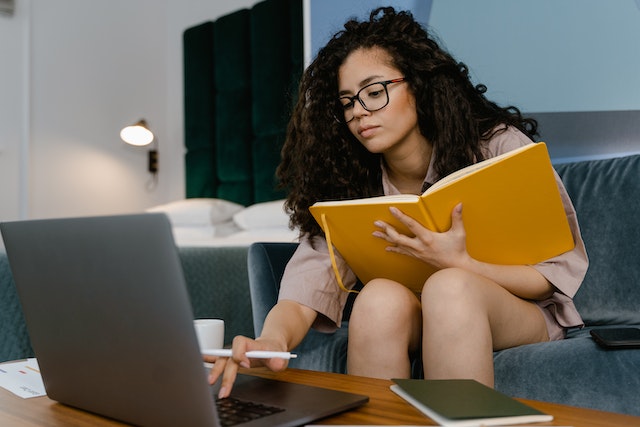 Person sitting on a couch, holding a notebook and using their laptop